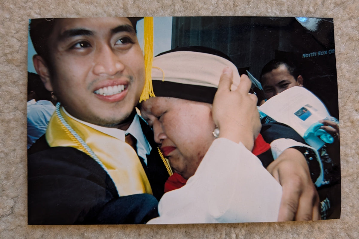 A photograph of Owntime Coffee's owner and his mother. The man is in a graduation cap and gown embracing his very proud mom, placed on a beige corkboard.