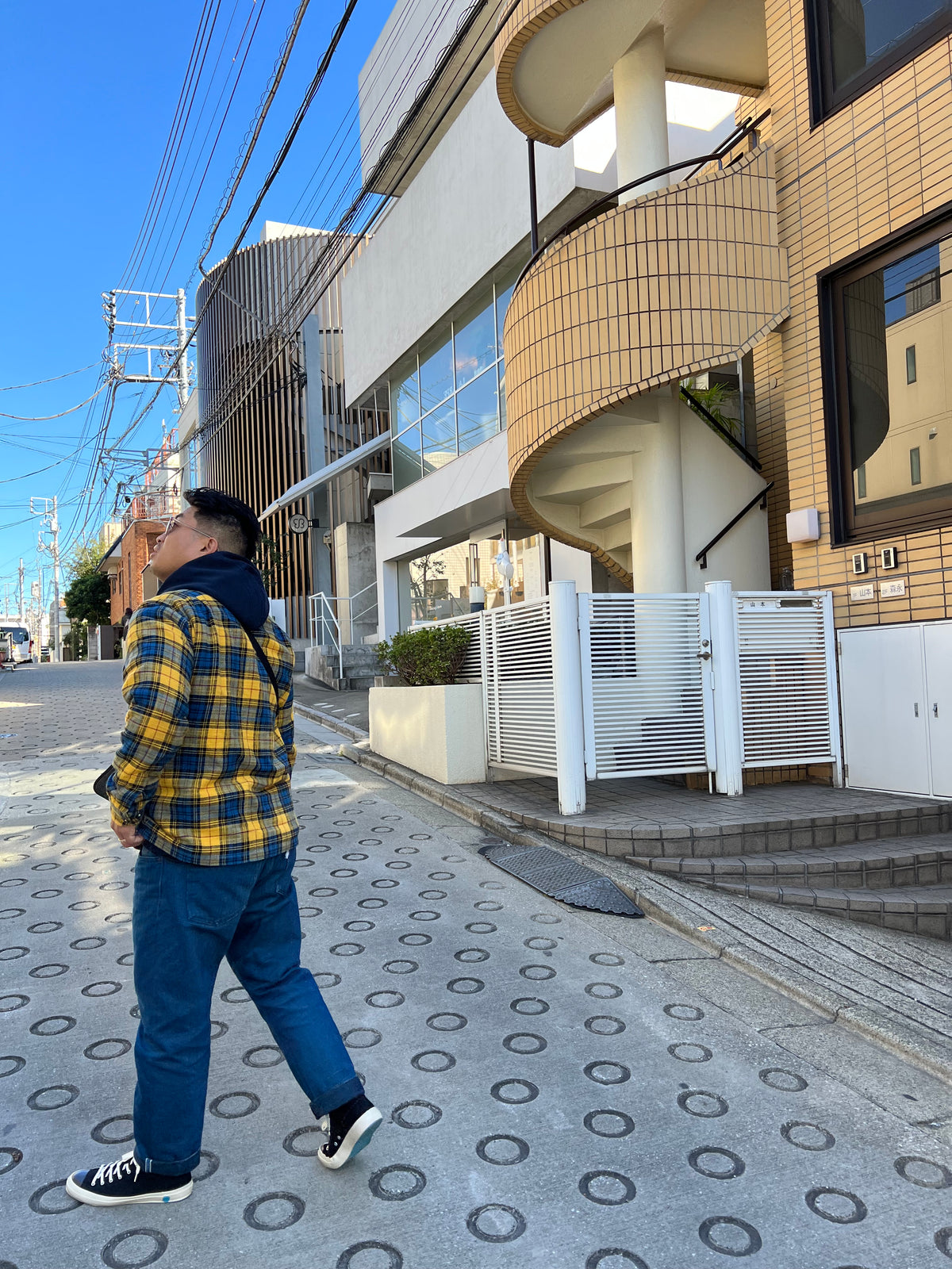 Person walking past modern building in Japan, wearing plaid