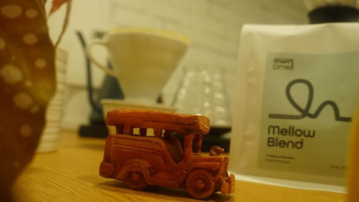 Small jeepney toy on a wooden coffee bar with a special Mellow Blend bag made for Mellow & Barbers in the background.