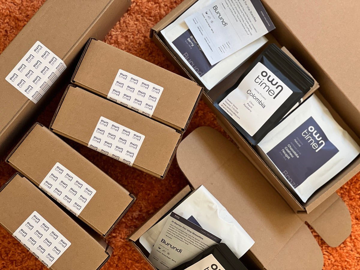 An overhead flat-lay of multiple brown cardboard boxes and an open box containing coffee bags and printed inserts. The visible product packaging includes bags labeled 'owntime'
